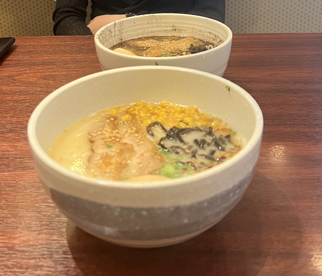 Two steaming bowls of ramen, one with corn and seaweed, on a wooden table.