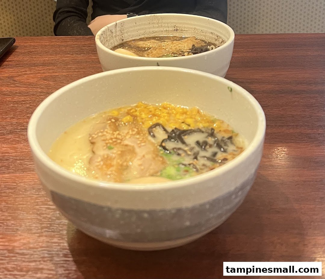 Two steaming bowls of ramen, one with corn and seaweed, on a wooden table.