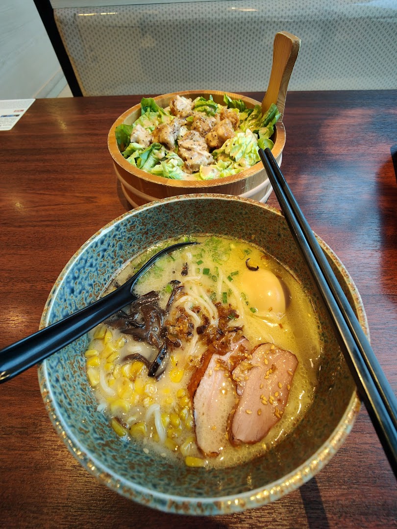 A close-up of a delicious ramen bowl with duck and corn, alongside a chicken salad.