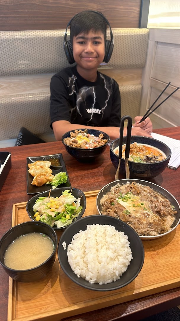 A young boy enjoys a delicious Japanese meal set with gyudon, ramen, and gyoza at Tokyo Shokudo.
