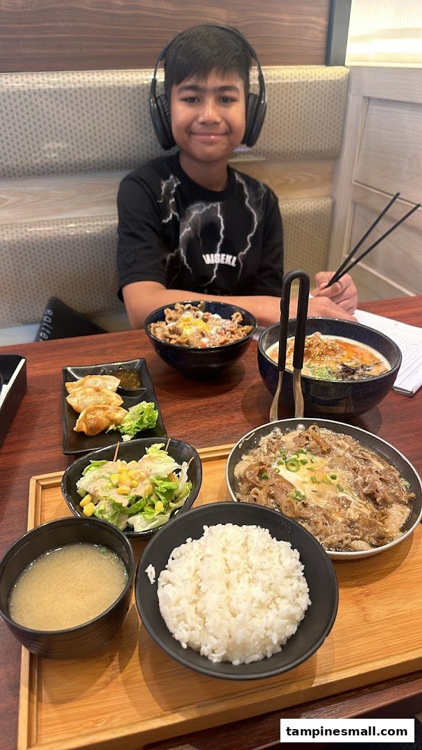 A young boy enjoys a delicious Japanese meal set with gyudon, ramen, and gyoza at Tokyo Shokudo.