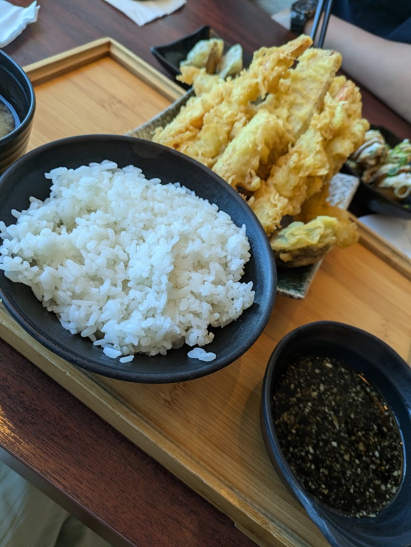 A close-up of a Japanese meal featuring crispy tempura, white rice, and a dipping sauce on a wooden tray.