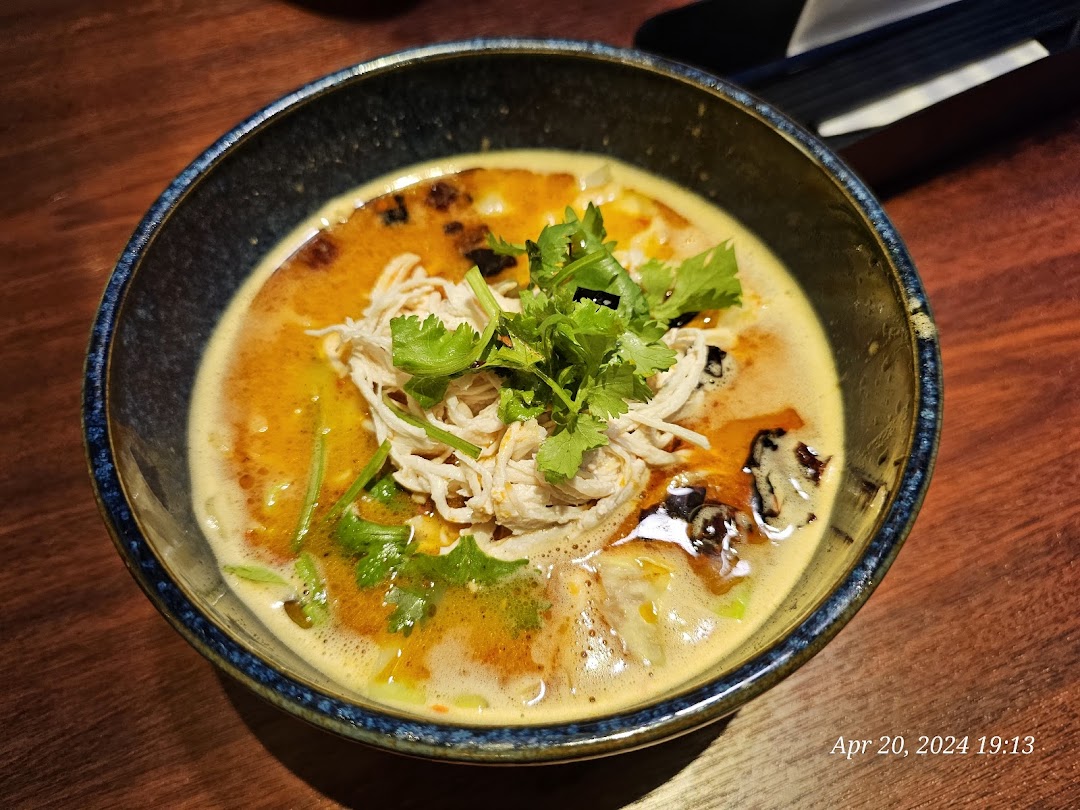 A close-up of a vibrant bowl of ramen or soup with shredded chicken and fresh cilantro.