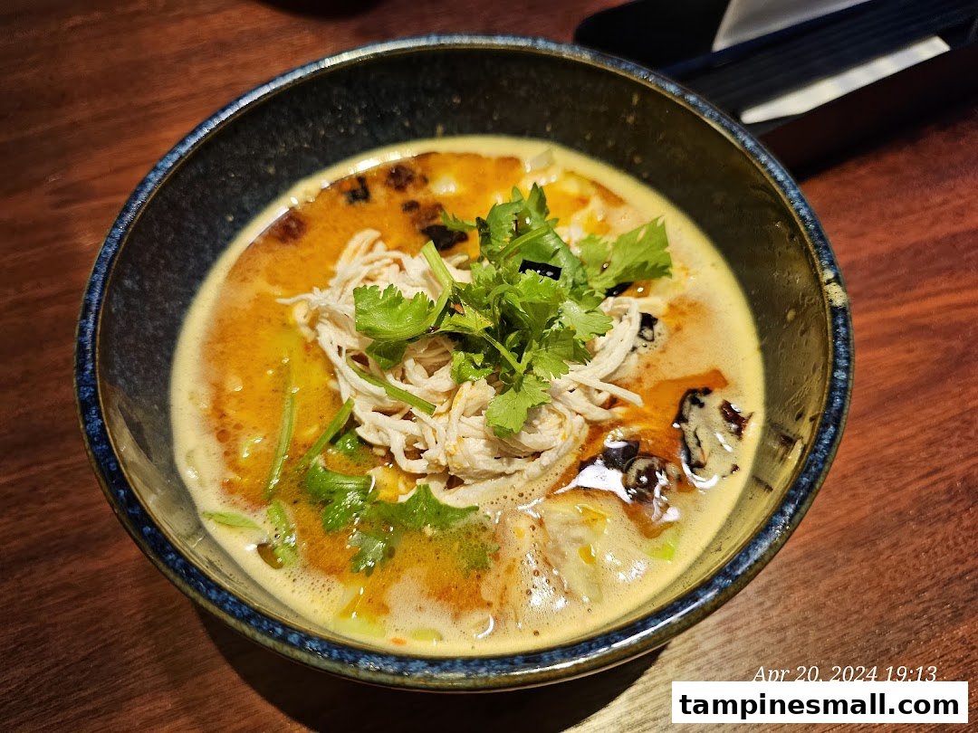 A close-up of a vibrant bowl of ramen or soup with shredded chicken and fresh cilantro.
