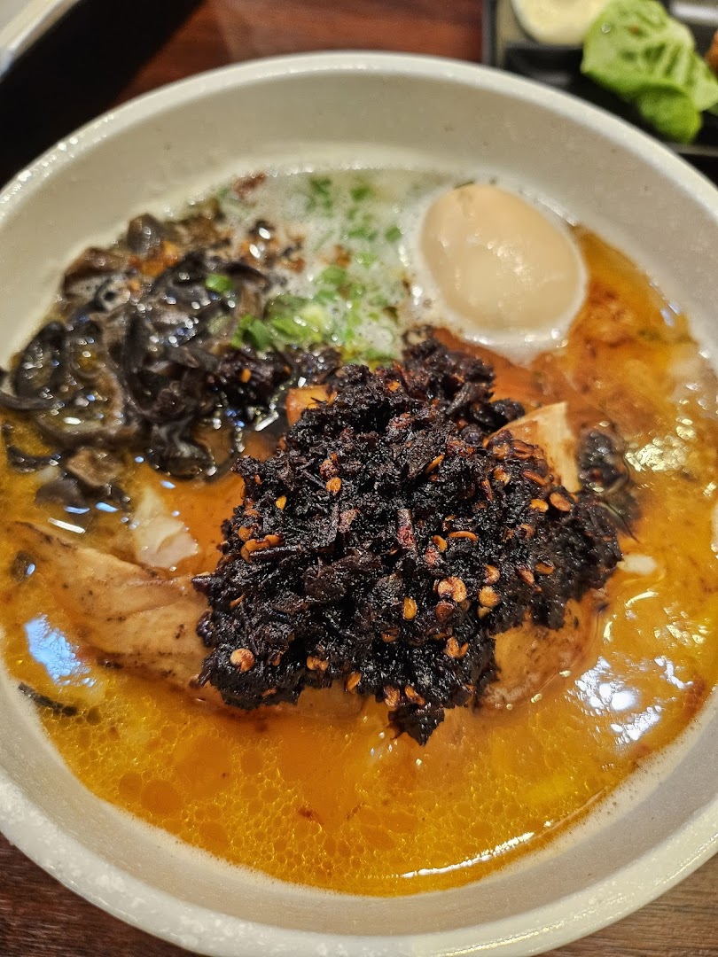 A close-up of a vibrant ramen or noodle dish with a rich broth, chili oil, a soft-boiled egg, and mushrooms.