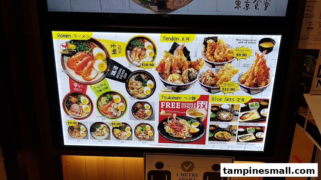 A brightly lit menu board showcasing various Japanese ramen, tendon, tsukemen, and rice sets with prices.