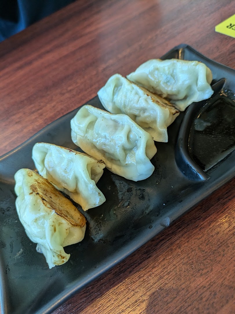 A plate of five pan-fried dumplings (gyoza) with dipping sauce on a dark platter.