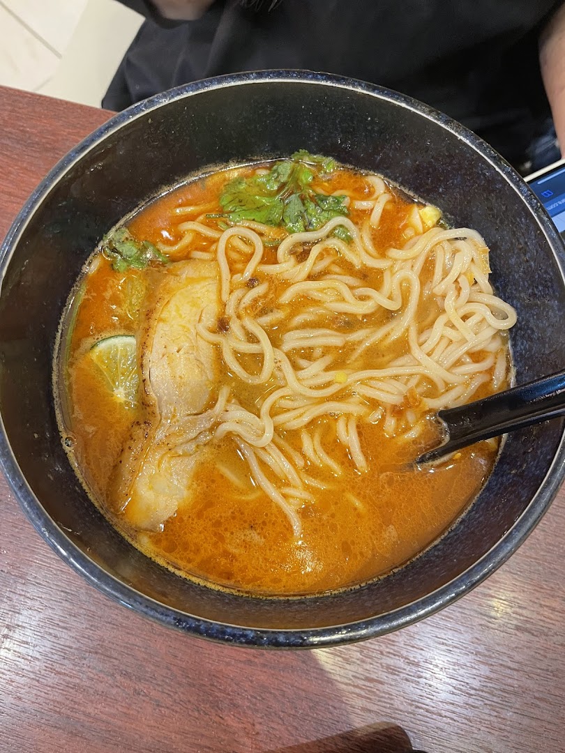 A close-up of a vibrant bowl of ramen with noodles, rich broth, meat, and fresh herbs.