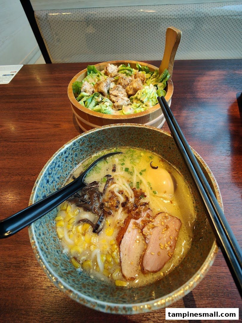 A close-up of a delicious ramen bowl with duck and corn, alongside a chicken salad.