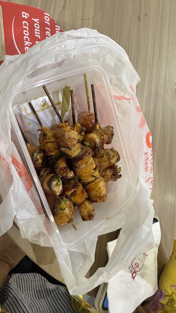 A plastic container filled with various grilled skewers, including chicken and vegetables, inside a plastic bag.