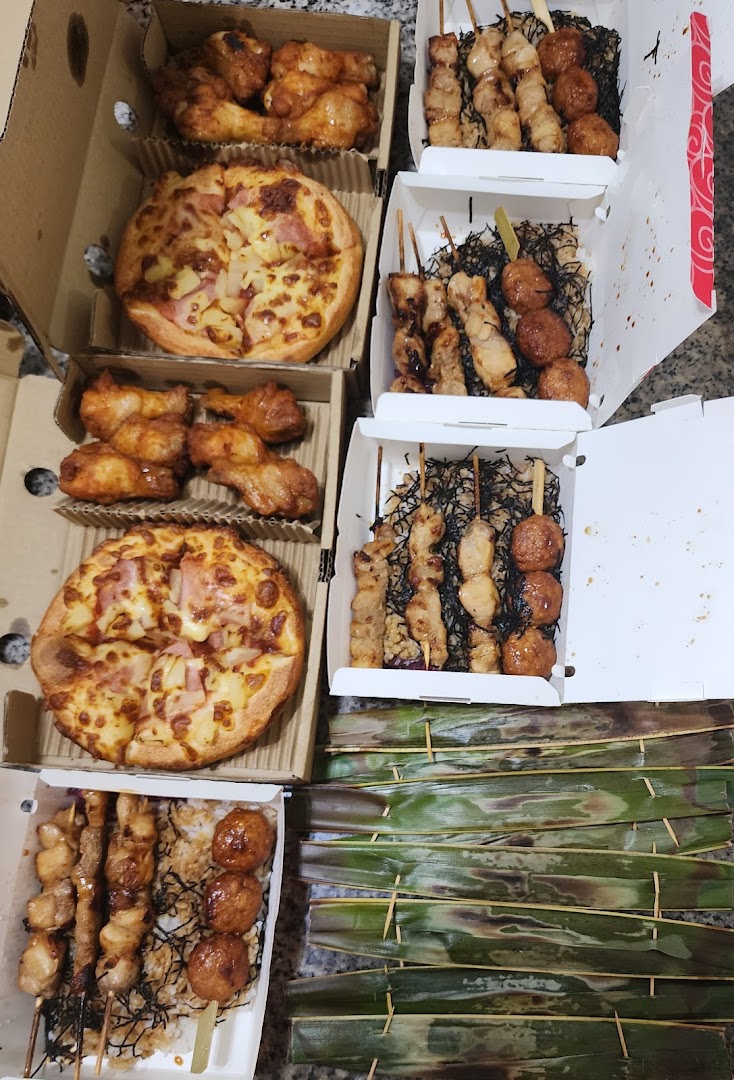 A spread of delicious takeout food including pizzas, chicken wings, and yakitori skewers in boxes.