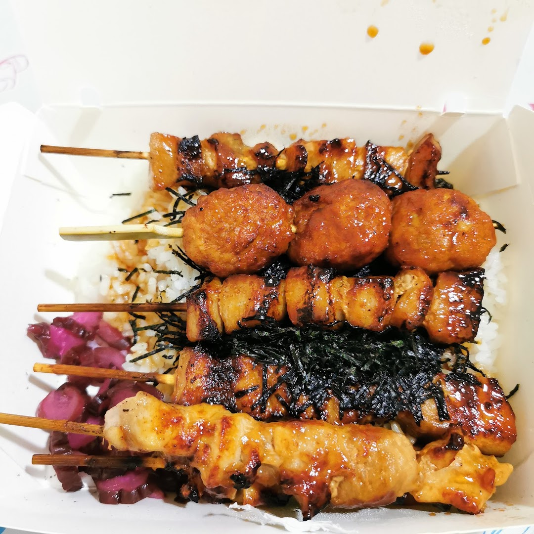 A bento box filled with grilled skewers (yakitori and tsukune) over rice, garnished with seaweed and pickles.