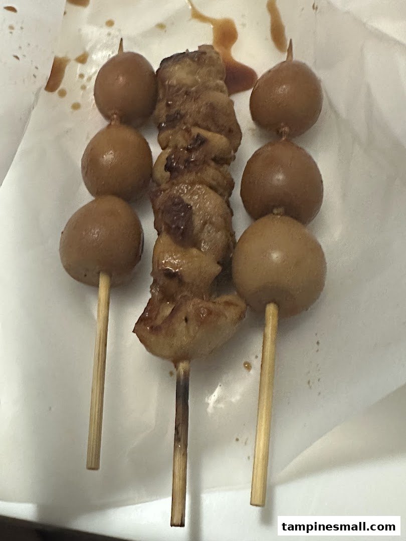 Close-up of three skewers, one with grilled chicken and two with quail eggs, served on white paper.