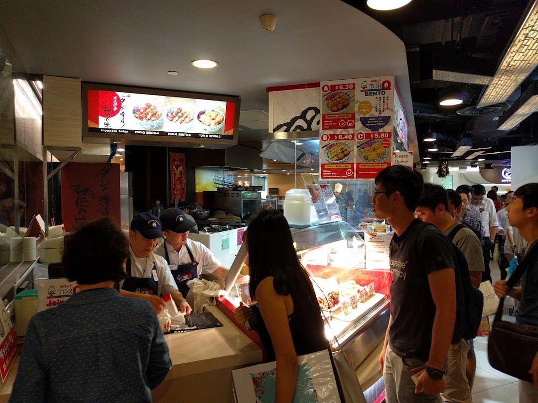 Customers queueing at the counter of TORI-Q, a Japanese food stall, with menu boards visible.