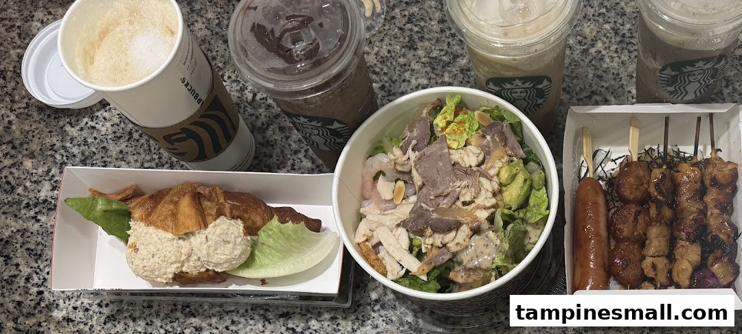 A diverse spread of takeout food and drinks, including skewers, a salad, a croissant sandwich, and Starbucks beverages.
