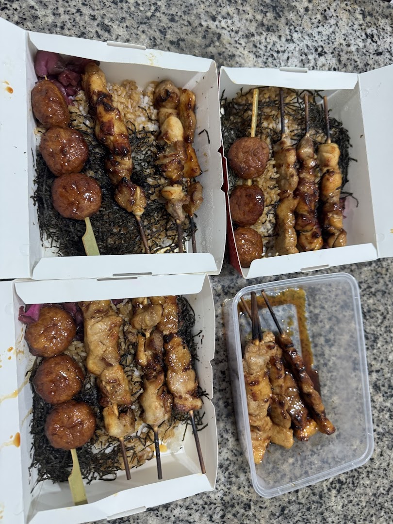 Multiple bento boxes filled with grilled skewers, meatballs, and rice, ready for takeaway.