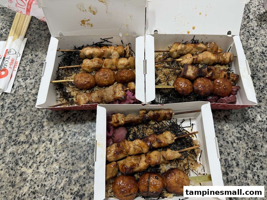 Three bento boxes filled with grilled yakitori skewers, rice, and seaweed, ready for takeaway.