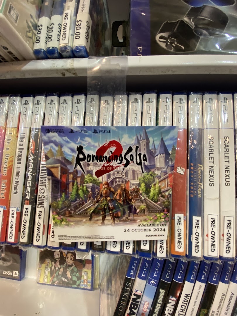 Shelves filled with video games, including PS4 and PS5 titles, and a Romancing SaGa promotional poster.