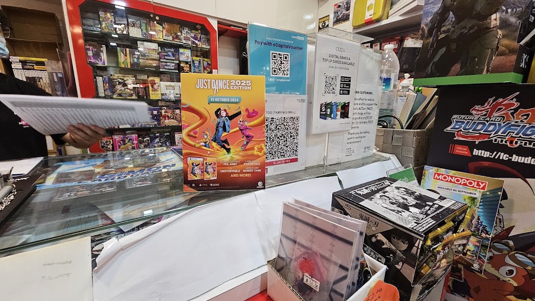 A vibrant retail shop counter displaying video games, card games, and promotional materials for new releases.
