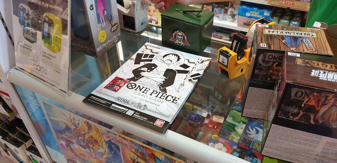 A retail display counter showcasing anime merchandise, card games, and digital bracelets from 'Toy Or Game' shop.