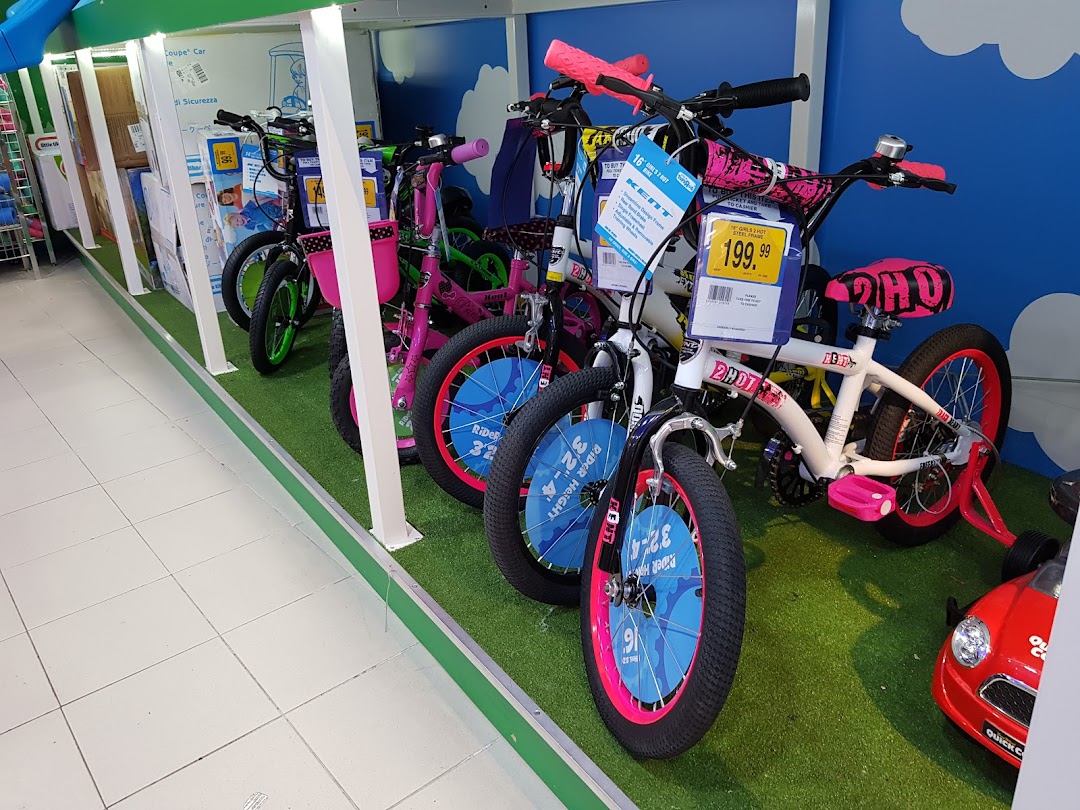 A vibrant display of children's bicycles, including pink and white models, on a green turf-like floor at ToysRUs.