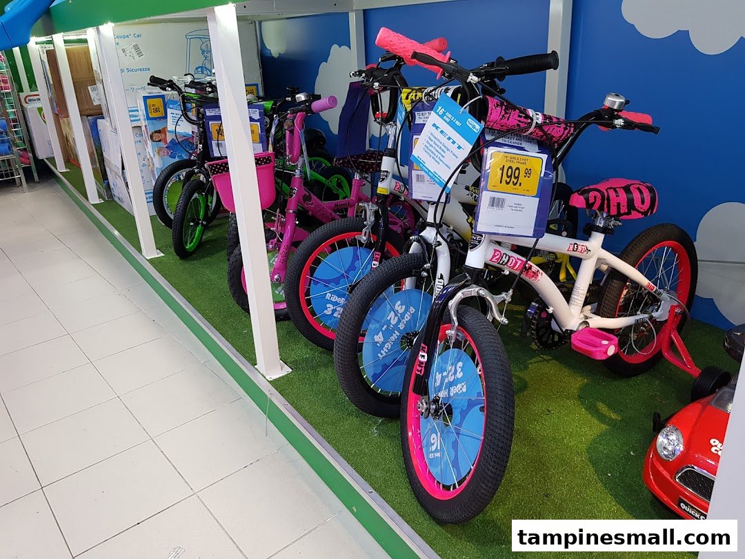 A vibrant display of children's bicycles, including pink and white models, on a green turf-like floor at ToysRUs.