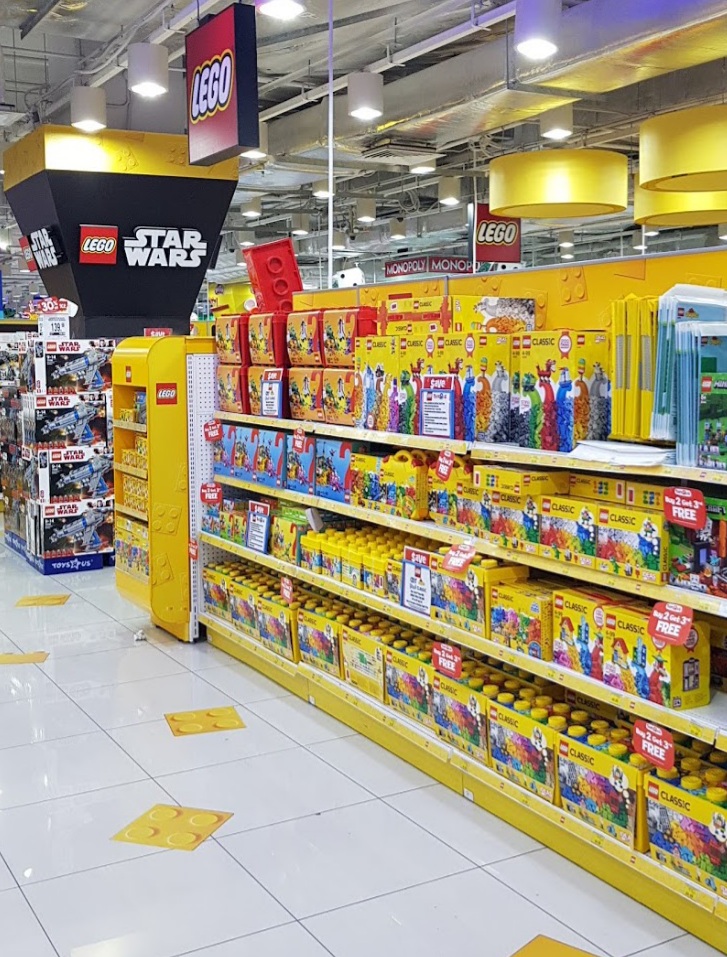 A brightly lit aisle in ToysRUs, showcasing shelves filled with various LEGO sets, including Classic and Star Wars themes.