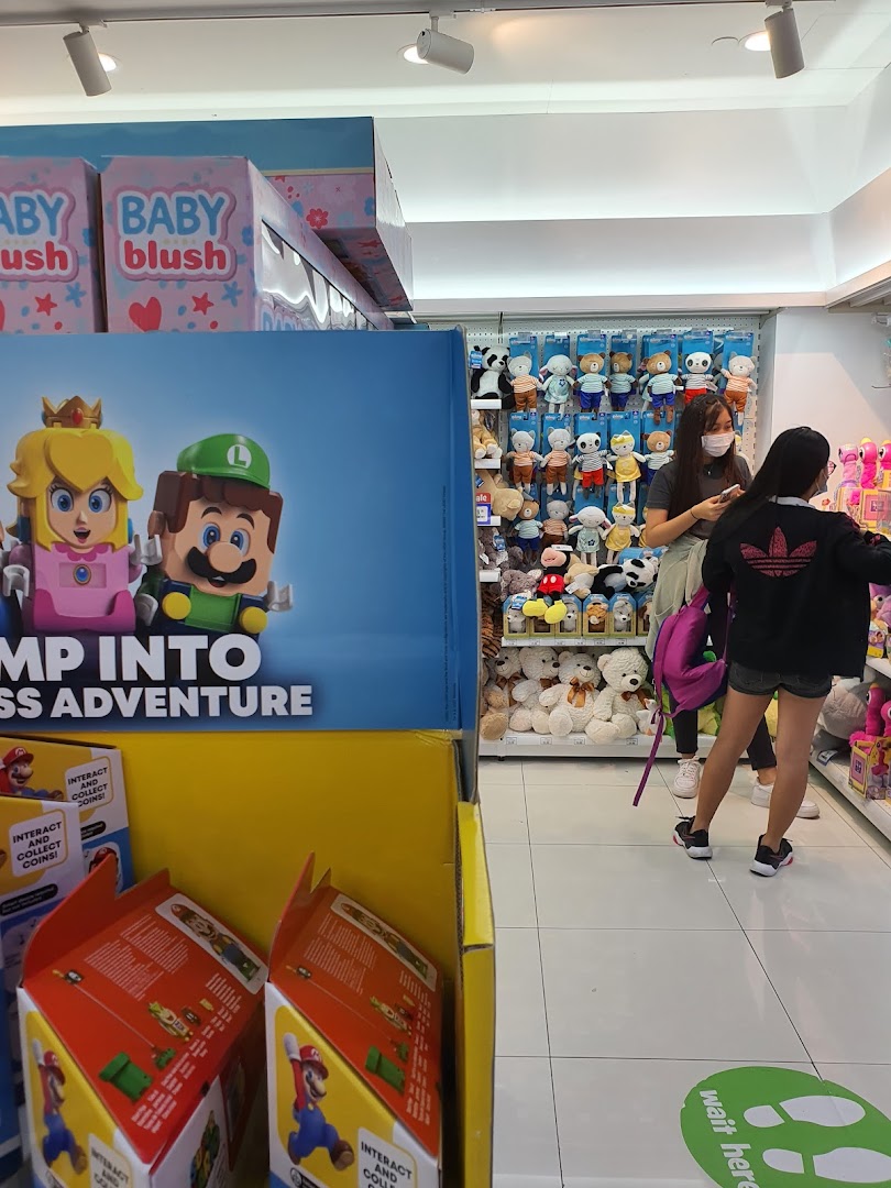 An aisle at ToysRUs featuring Super Mario displays, plush toys, and shoppers exploring the wide selection.