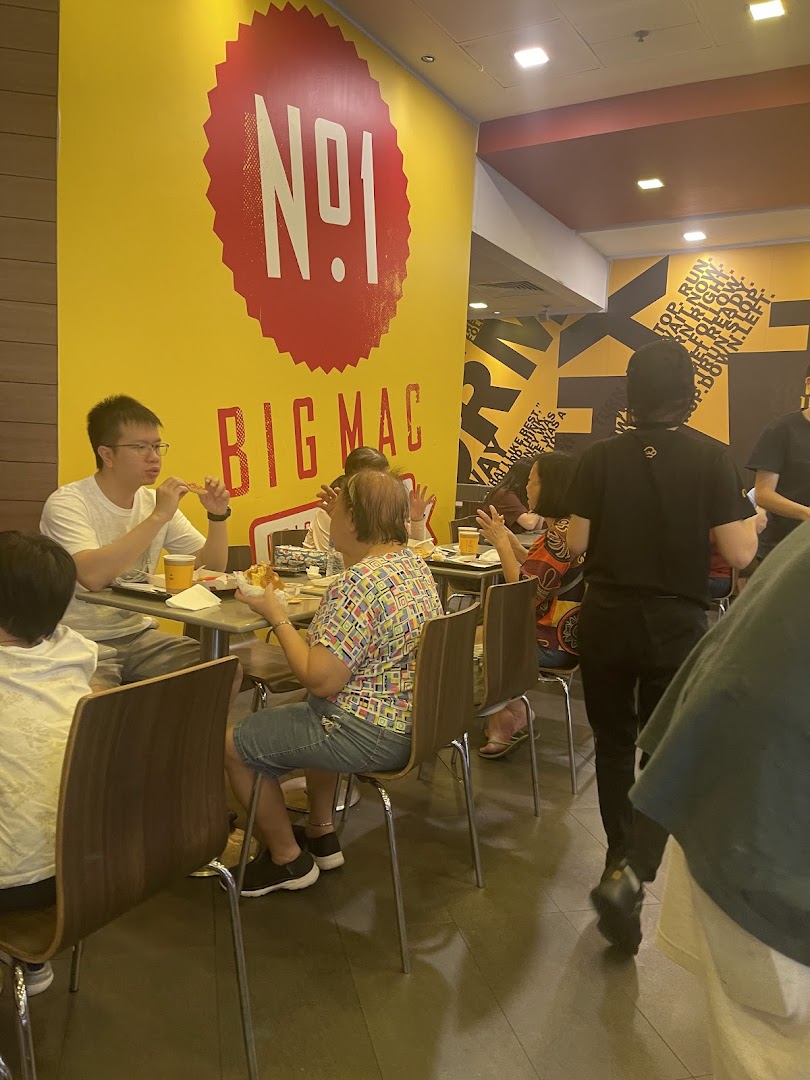 Customers enjoy meals inside a bustling fast-food restaurant with vibrant yellow walls and bold graphics.