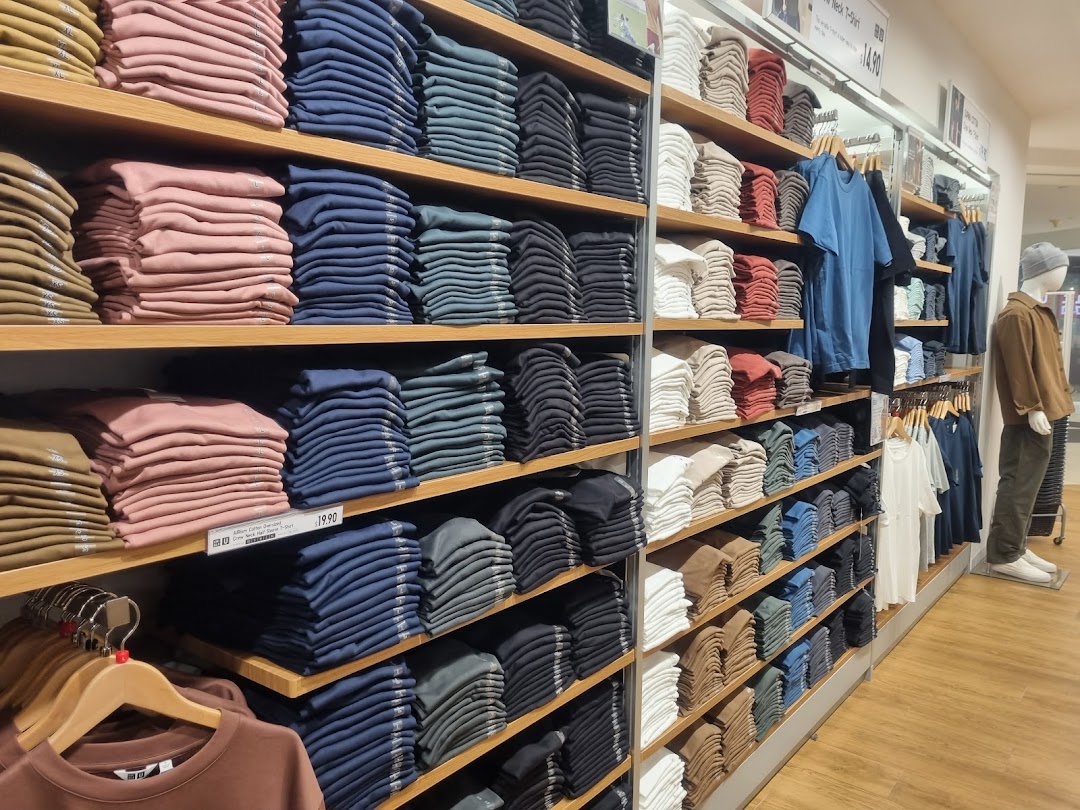 Neatly folded apparel in various colors displayed on shelves inside a UNIQLO store.