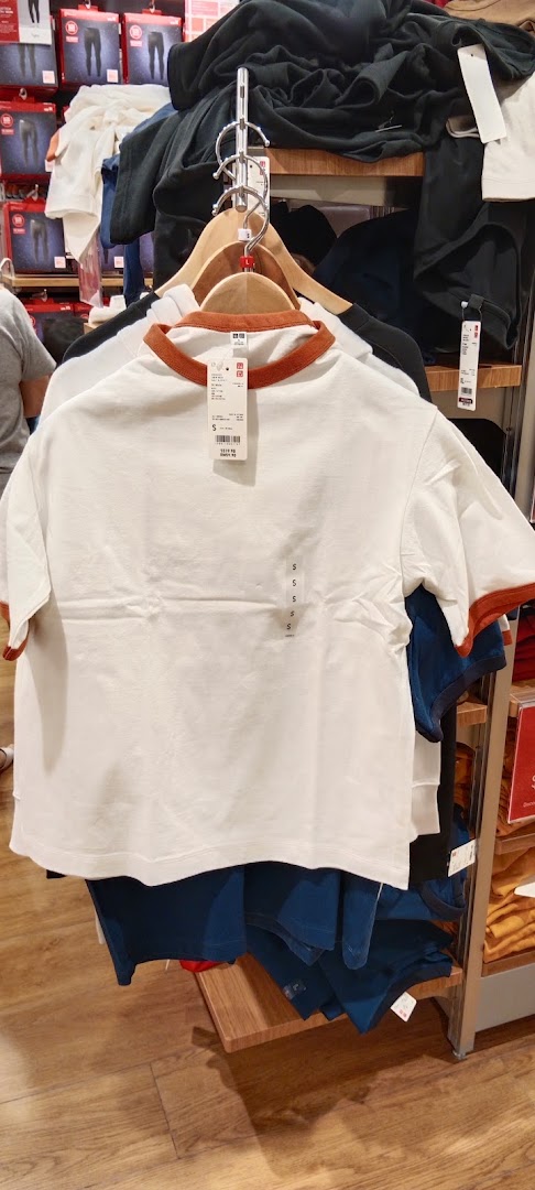 A white UNIQLO t-shirt with brown trim hangs on a display rack inside the store.