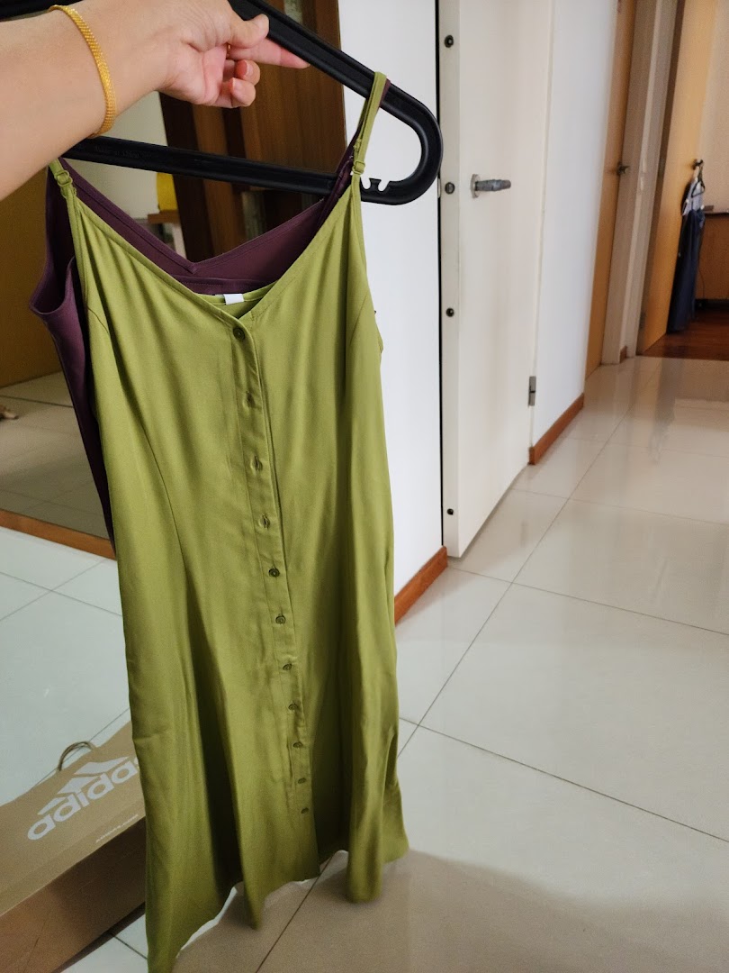 A hand holds up two dresses, one olive green and one purple, on hangers.