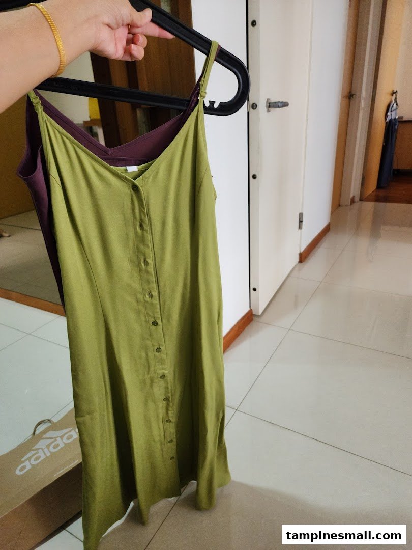 A hand holds up two dresses, one olive green and one purple, on hangers.