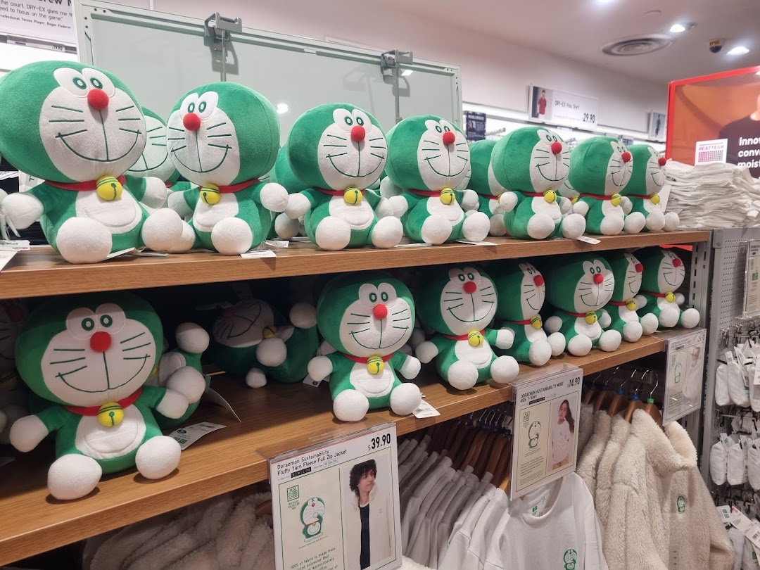 Shelves filled with green Doraemon plush toys and related apparel at UNIQLO.
