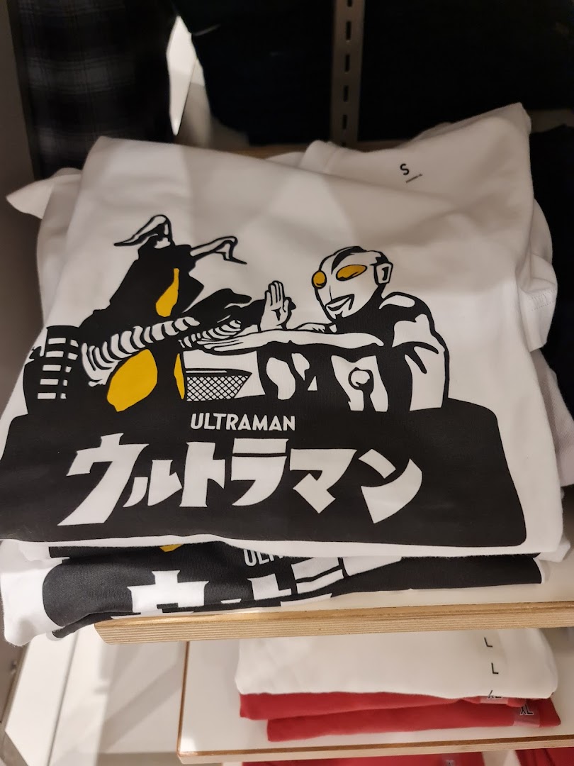 A white graphic t-shirt featuring an Ultraman design, stacked on a shelf in a retail store.