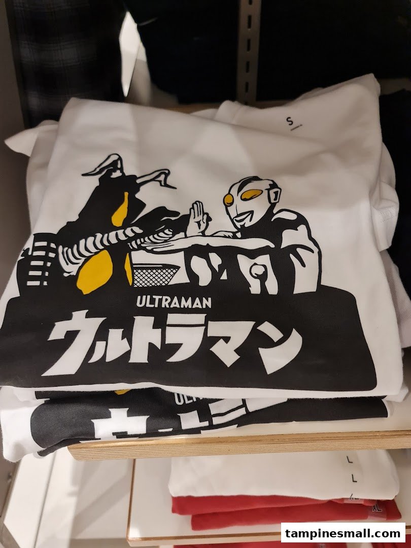 A white graphic t-shirt featuring an Ultraman design, stacked on a shelf in a retail store.