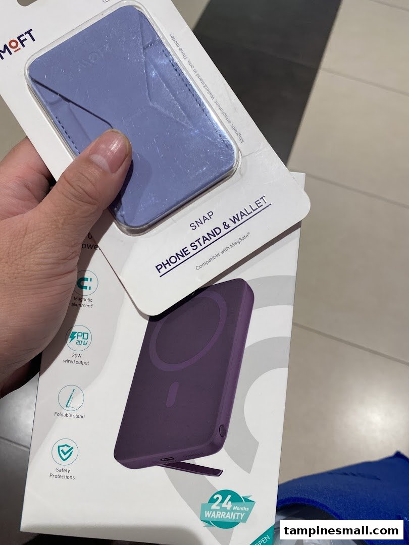 A hand holds two packaged tech accessories: a purple phone stand/wallet and a power bank.