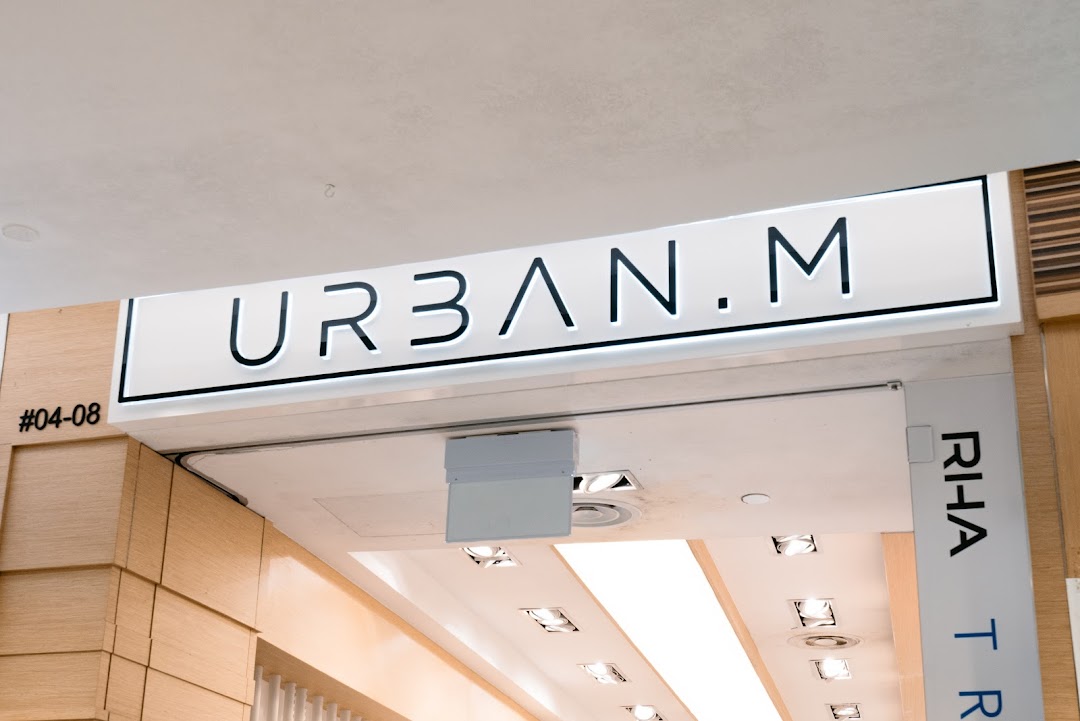 An illuminated 'URBAN.M' sign above a modern shop entrance, with store number #04-08 visible.