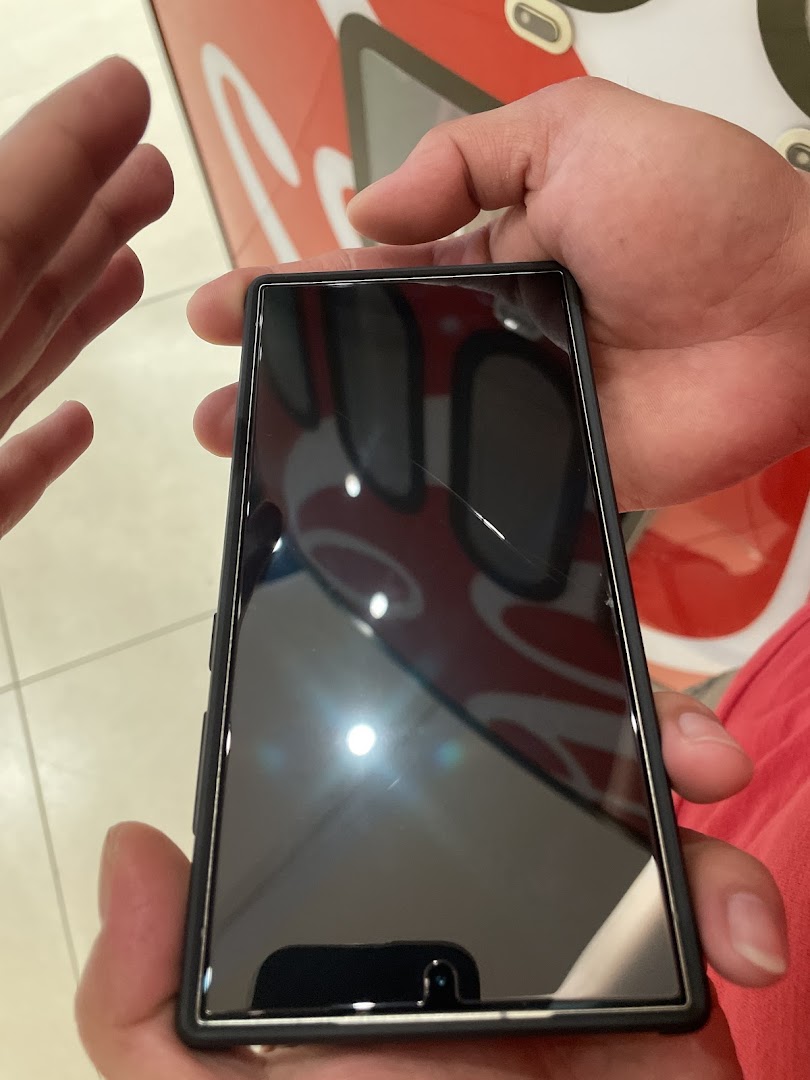 A person holds a smartphone with a cracked screen protector, reflecting the shop's interior.