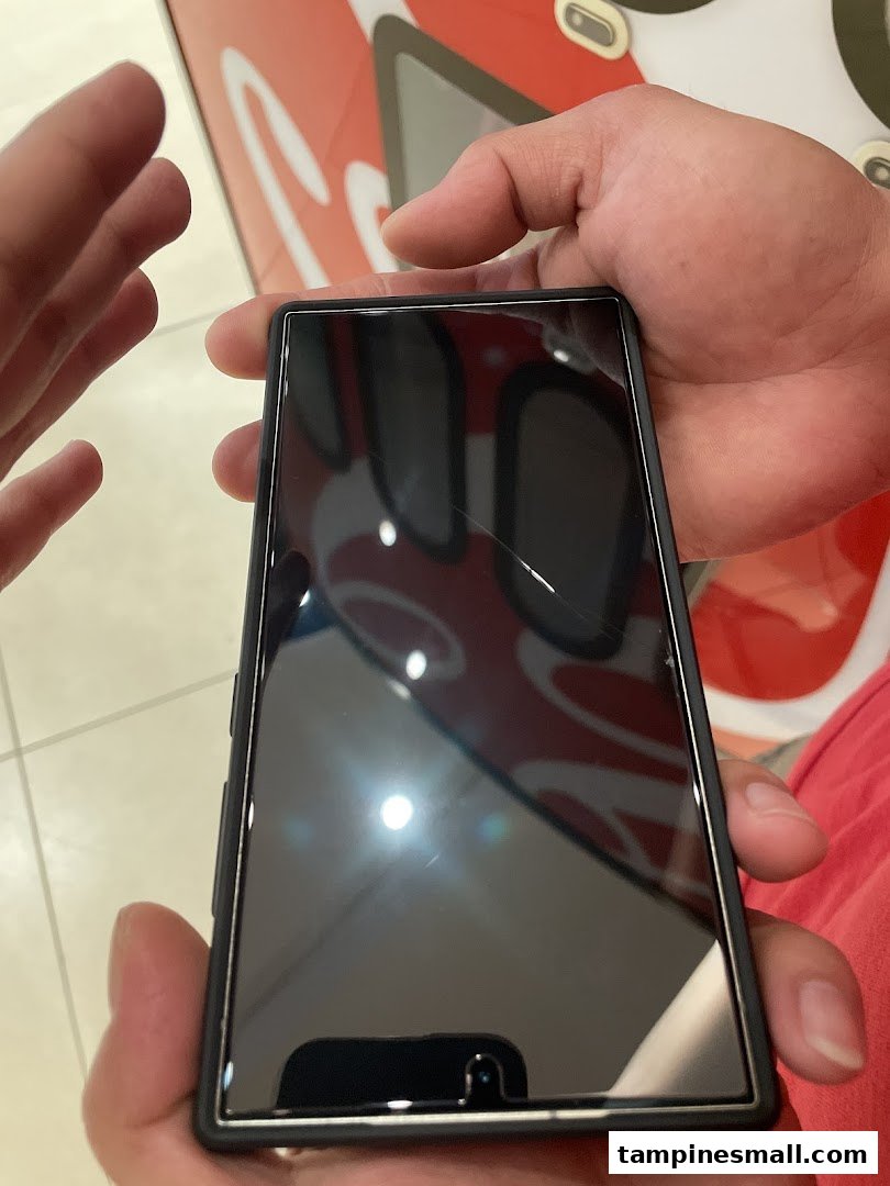 A person holds a smartphone with a cracked screen protector, reflecting the shop's interior.