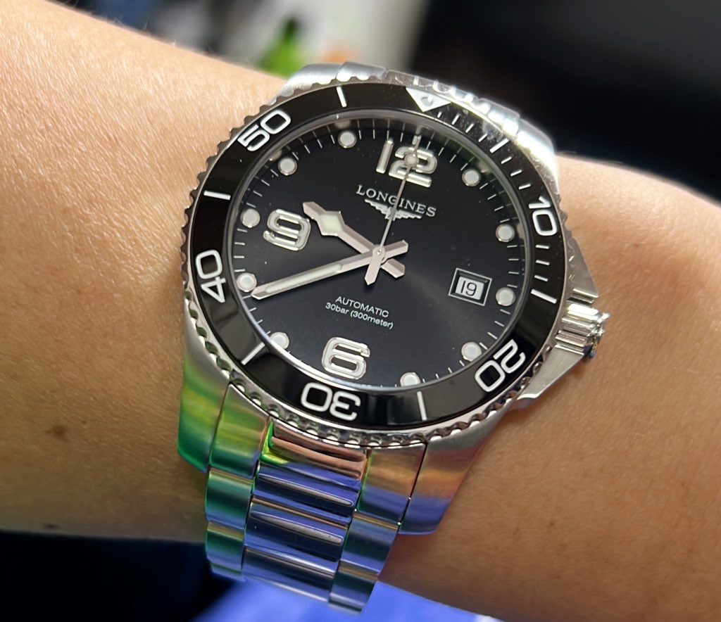 A close-up of a Longines automatic dive watch with a black dial and steel bracelet on a wrist.