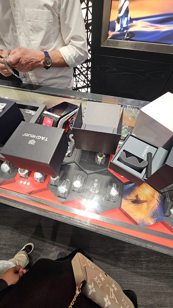 A customer views luxury watches in a display case at Vincent Watch, with open TAG Heuer boxes.