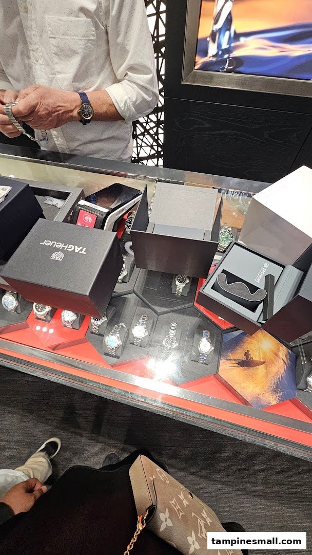 A customer views luxury watches in a display case at Vincent Watch, with open TAG Heuer boxes.