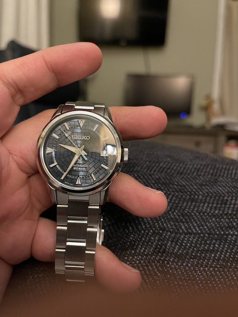 A hand holds a silver Seiko automatic watch with a distinctive patterned blue dial.