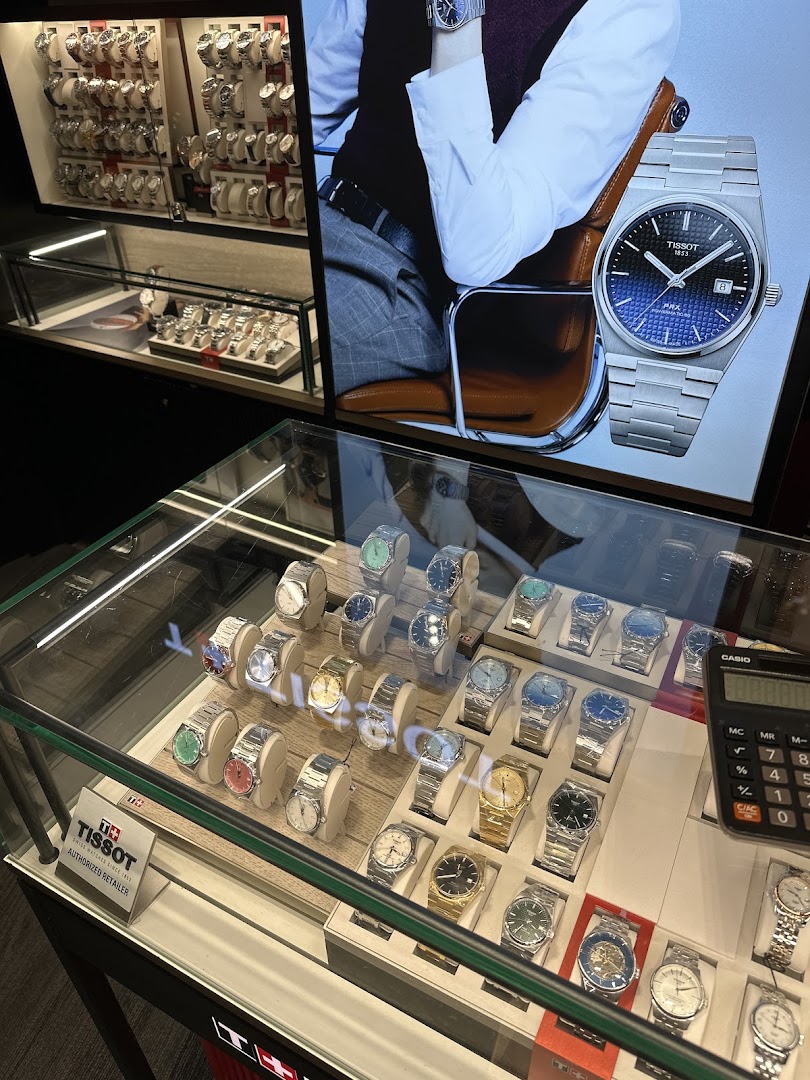 Interior view of a watch shop showcasing various timepieces in display cases and a large Tissot advertisement.