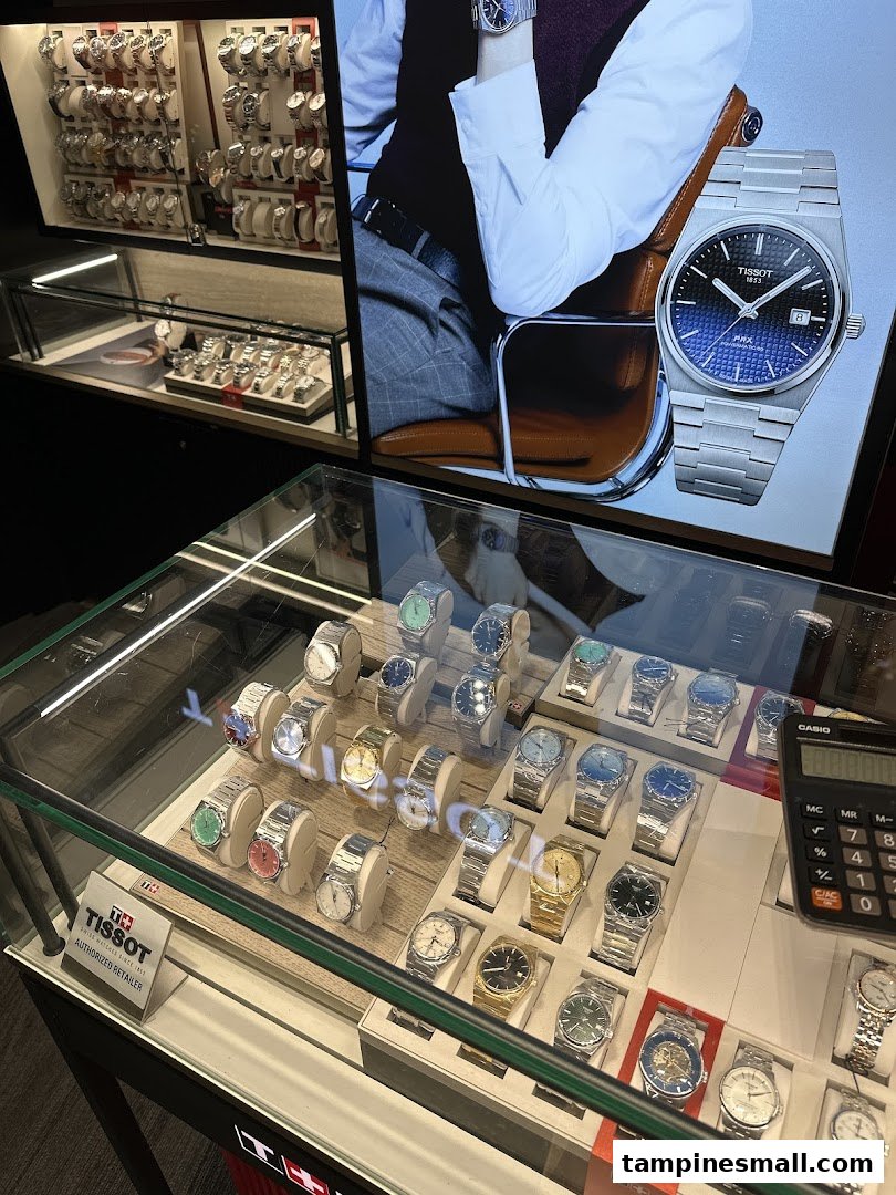 Interior view of a watch shop showcasing various timepieces in display cases and a large Tissot advertisement.