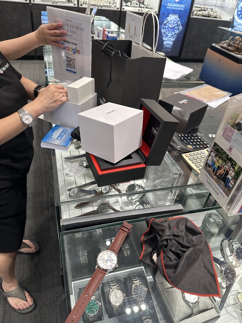 A staff member at Vincent Watch handles watch boxes (Seiko, Tissot) at a display counter, showcasing premium timepieces.