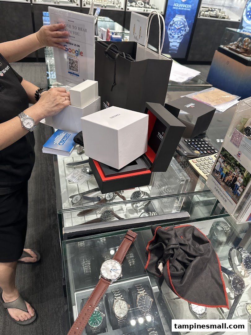 A staff member at Vincent Watch handles watch boxes (Seiko, Tissot) at a display counter, showcasing premium timepieces.