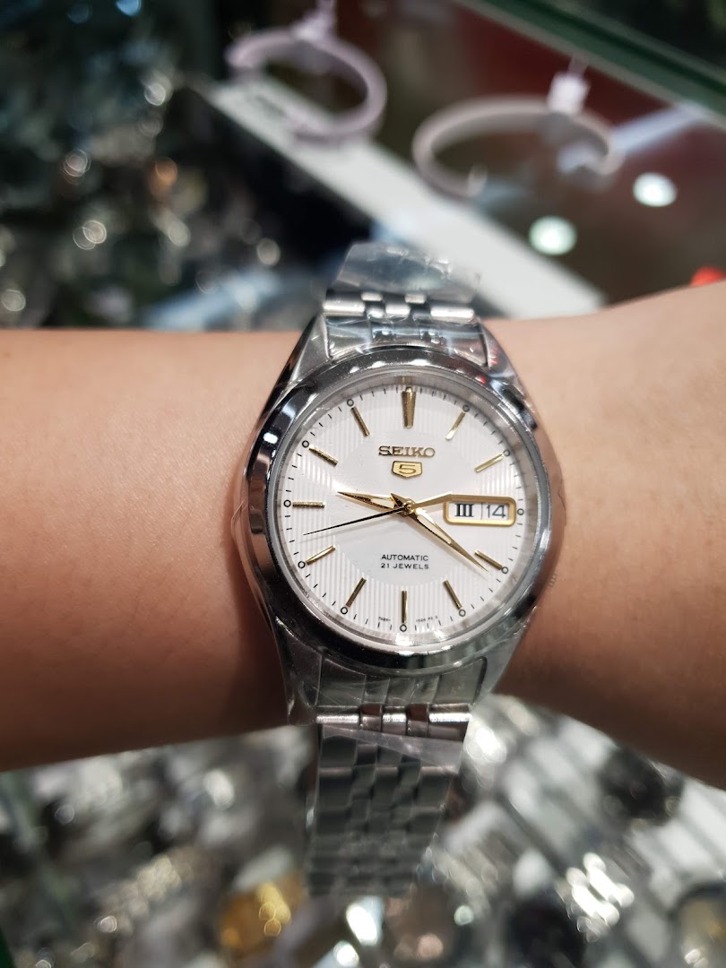 A close-up of a silver Seiko 5 automatic watch with a white dial on a wrist.