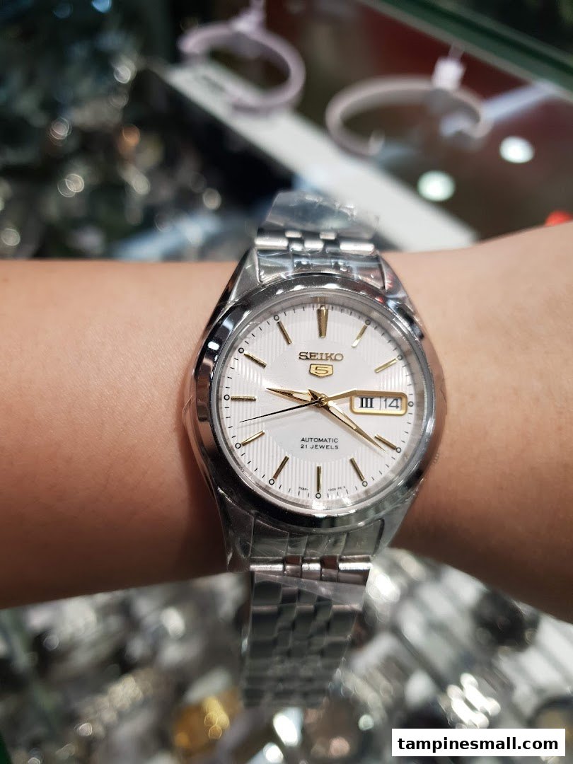 A close-up of a silver Seiko 5 automatic watch with a white dial on a wrist.